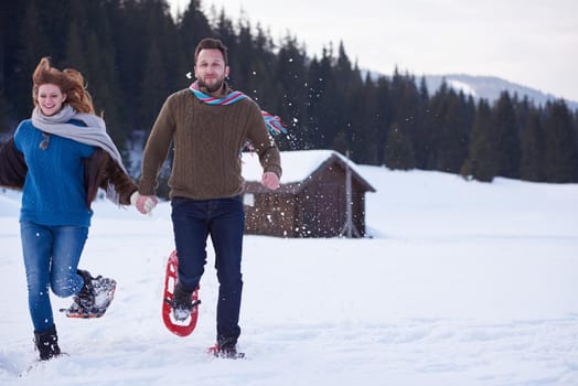 happy young  couple having fun and walking in snow shoes. Romantic winter relaxation scene