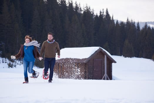 happy young  couple having fun and walking in snow shoes. Romantic winter relaxation scene