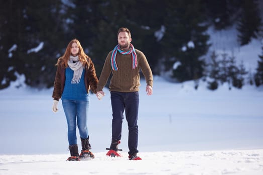 happy young  couple having fun and walking in snow shoes. Romantic winter relaxation scene