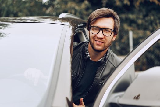 Stylish man in glasses sits in a car, close up portrait