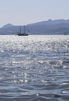 Blue sea waves sparkling in the sun and a yacht. Summer holidays concept