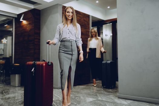 Two young women in formal clothes entering hotel lobby. Business trip concept