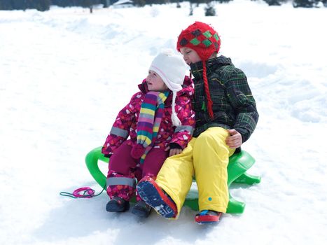 portrait of boy and baby girl on winter vacation sitting on sleddge with fresh snow on beautiful sunny day