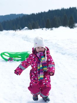 little baby girl have fun on fresh snow and slide on sleddges at beautiful sunny winter day