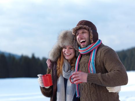 portrait of happy young couple outdoor on winter day drinking warm tea with fresh snow in background