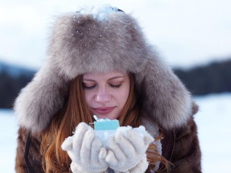 happy young redhair girl  with gift and snow in  hands. Christmas and winter shopping concept, forest in background