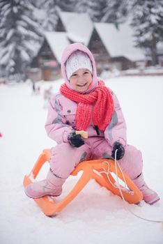 portrait of cute little girl child sitting on sledges at winter day with fresh snow,  eat cookies and have break