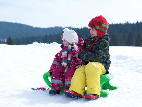 portrait of boy and baby girl on winter vacation sitting on sleddge with fresh snow on beautiful sunny day