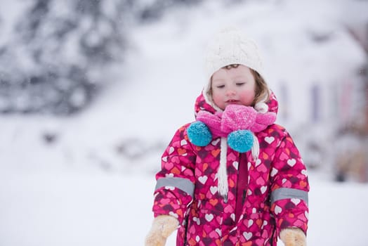 portrait of happy smiling little girl outdoors, having fun and playing on fresh snow on snowy  winter day