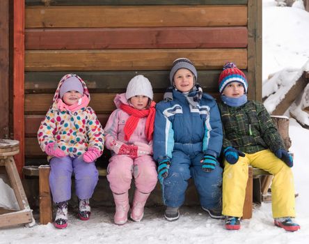 group portrait of kids, little child  group sitting together  in front of wooden cabin on vacation at beautiful winter  day with fresh snow