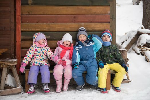 group portrait of kids, little child  group sitting together  in front of wooden cabin on vacation at beautiful winter  day with fresh snow