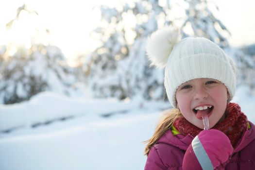 portrait of cute little girl  while eating icicle  on beautiful winter day with fresh snow