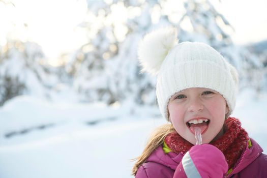 portrait of cute little girl  while eating icicle  on beautiful winter day with fresh snow