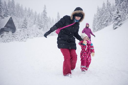 happy family on winter vacation, portrait of mother  and cute little girl have fun and slide while snow falkes falling