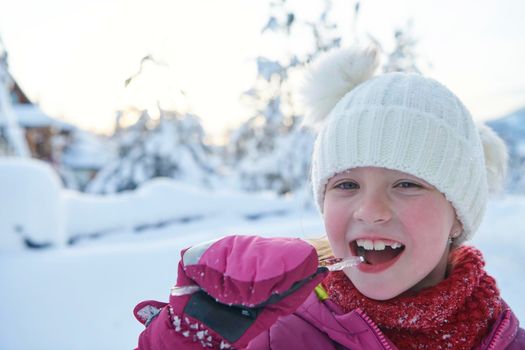 portrait of cute little girl  while eating icicle  on beautiful winter day with fresh snow