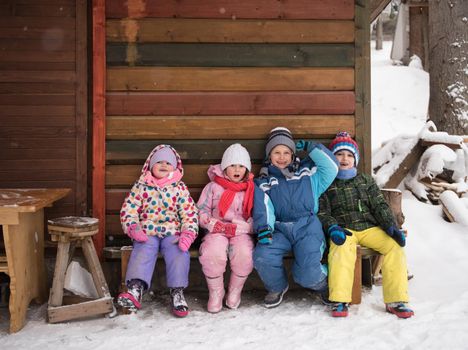 group portrait of kids, little child  group sitting together  in front of wooden cabin on vacation at beautiful winter  day with fresh snow