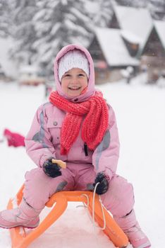 portrait of cute little girl child sitting on sledges at winter day with fresh snow,  eat cookies and have break