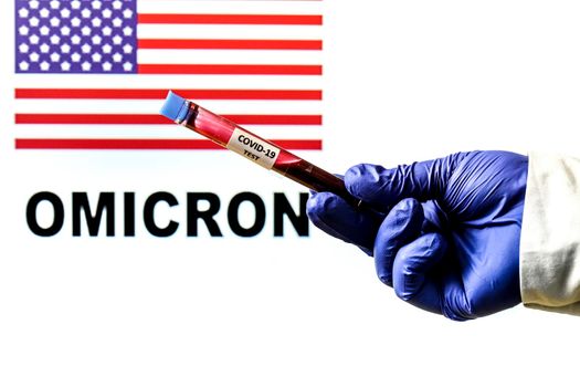Hand holding test tube of covid-19 virus on white background with United States flag and Omicron word written on it