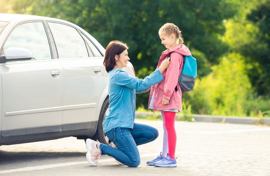 Smiling mother bringing daughter back to school saying goodbye on car parking