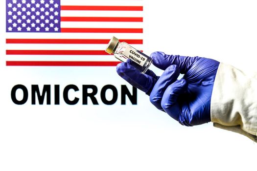 Hand holding vial with covid vaccine. United States flag and Omicron covid variant word written in the background