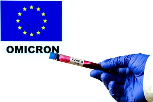 Hand holding test tube of covid-19 virus on white background with European flag and Omicron word written on it