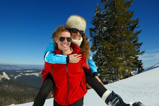 Happy young couple has fun on fresh snow at beautiful winter sunny day on vacation