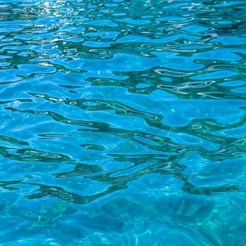 Turquoise sea waves in sunshine glow as surface background. Summer holidays and coastal nature concept