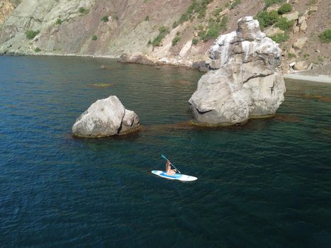 Young attractive brunette woman in red swimsuit, swimming on kayak around volcanic rocks, like in Iceland. Back view. Christmas holiday vacation and travel concept.