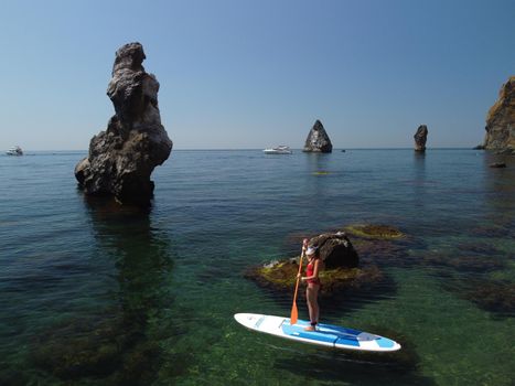 Young attractive brunette woman in red swimsuit, swimming on kayak around volcanic rocks, like in Iceland. Back view. Christmas holiday vacation and travel concept.