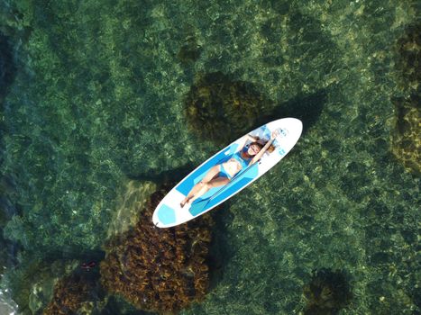 Young attractive brunette woman in red swimsuit, swimming on kayak around volcanic rocks, like in Iceland. Back view. Christmas holiday vacation and travel concept.