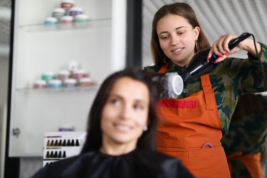 Portrait of smiling hairdresser using hairdryer for treatment with hair and being creative. Professional equipment for work with hair. Wellness concept