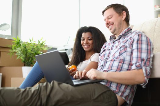 Portrait of friends sitting on carpet floor watching movie on laptop and laughing. Latino american woman eat apple. Spare time, friendship, leisure concept