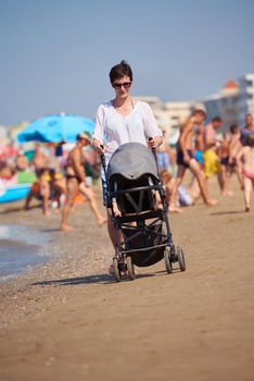 happy young mother walking on beach and push baby carriage