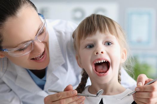 Portrait of cute kid visiting family doctor and open mouth pediatrician with tool check hurting throat. Healthcare, medicine, clinic, childhood concept