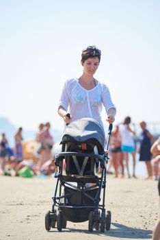 happy young mother walking on beach and push baby carriage