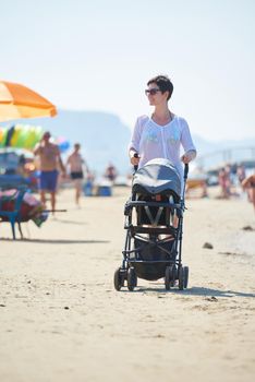 happy young mother walking on beach and push baby carriage