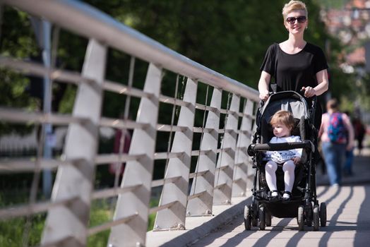 beautiful young mother with blond hair and sunglasses pushed her baby daughter in a stroller on a summer day