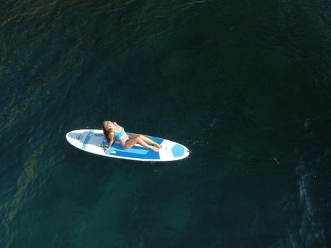 Young attractive brunette woman in red swimsuit, swimming on kayak around volcanic rocks, like in Iceland. Back view. Christmas holiday vacation and travel concept.