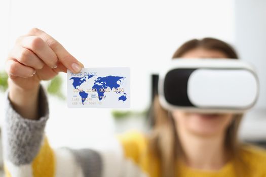 Close-up of young woman wearing virtual glasses and showing credit card. Payment via internet banking for participating in online game. Technology concept