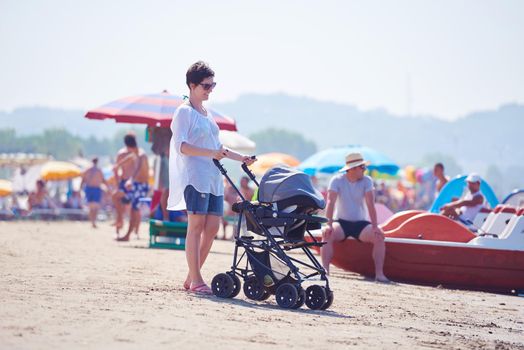 happy young mother walking on beach and push baby carriage