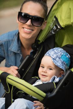 portrait of a beautiful young mother with sunglasses and a baby in a stroller on a sunny day in the park