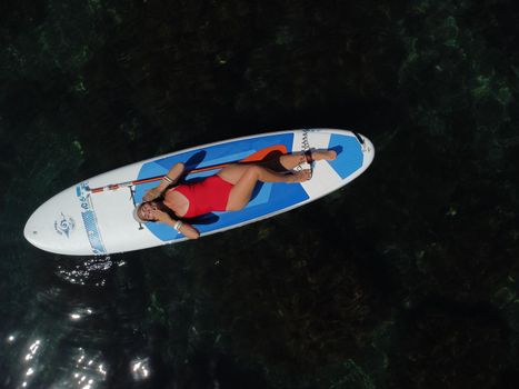 Young attractive brunette woman in red swimsuit, swimming on kayak around volcanic rocks, like in Iceland. Back view. Christmas holiday vacation and travel concept.