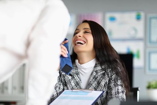Portrait of businesswoman flirting with corporate male worker touching his tie and laughing. Female boss start relationship at work. Office romance concept