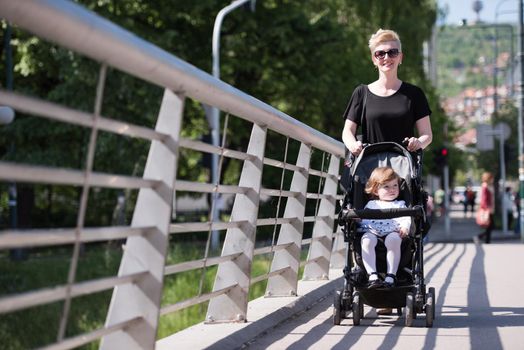 beautiful young mother with blond hair and sunglasses pushed her baby daughter in a stroller on a summer day