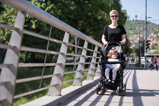 beautiful young mother with blond hair and sunglasses pushed her baby daughter in a stroller on a summer day