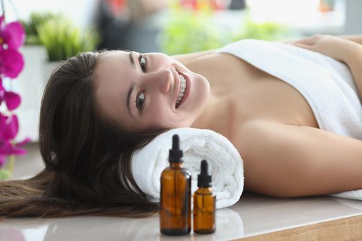 Portrait of smiling happy woman laying covered with towels in luxury spa centre. Rested female surrounded with beauty and smelly oils. Self care concept
