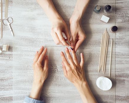 Mother and daughter do manicure, paint nails with varnish. Home care during quarantine, self-isolation. Top view of hands on table.