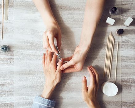 Mother and daughter do manicure, paint nails with varnish. Home care during quarantine, self-isolation. Top view of hands on table.