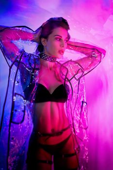 the slender woman in a swimsuit and a transparent raincoat in neon light