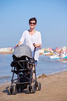 happy young mother walking on beach and push baby carriage